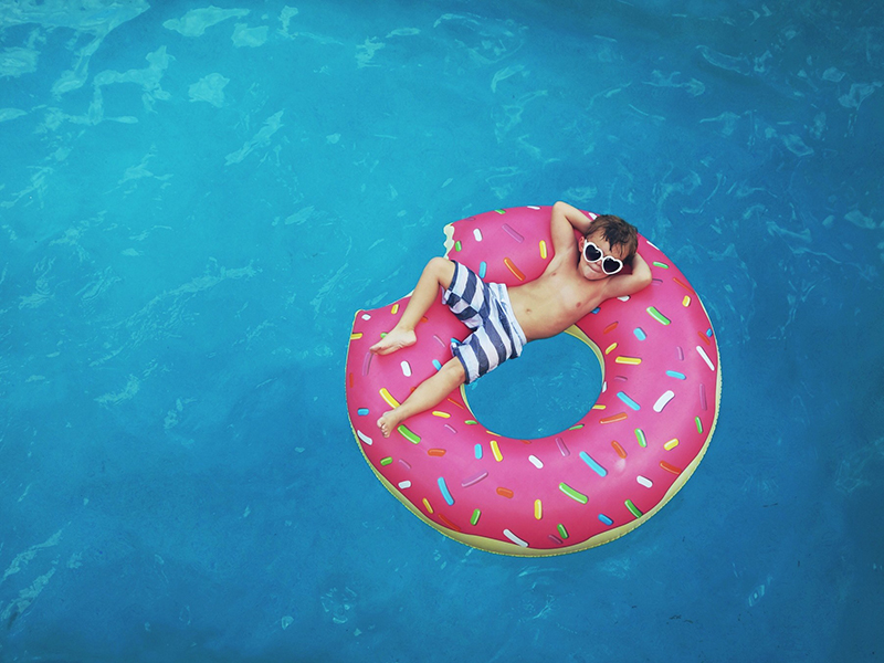 Boy relaxing on a pink donut float in swimming pool
