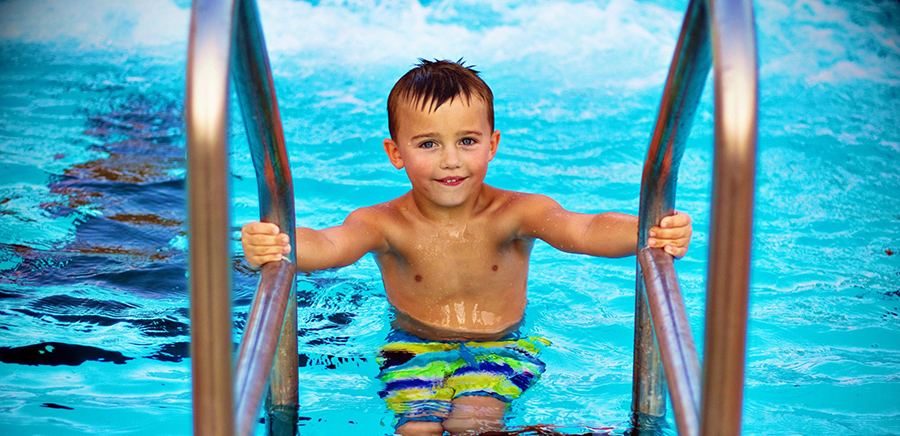 Child smiling while exiting swimming pool using pool ladder
